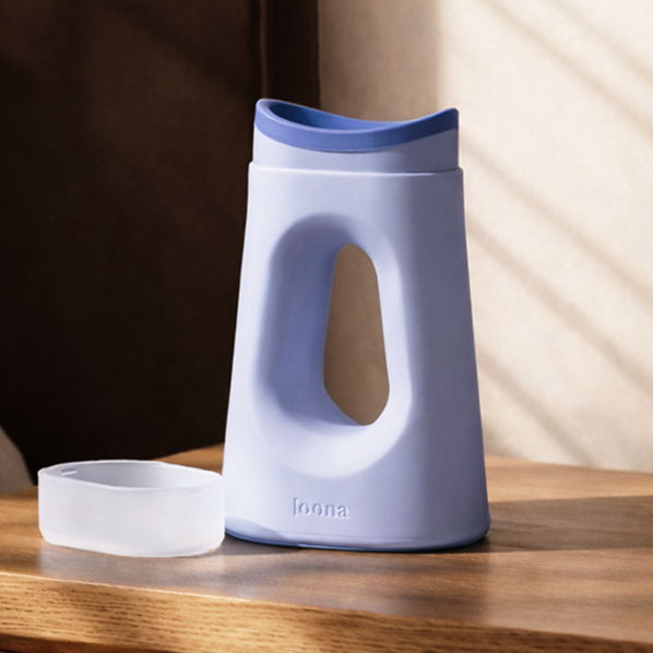 Periwinkle Loona female urinal on a wooden bedside table with its frosted snap-close lid resting beside it