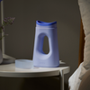 Periwinkle Loona on a round white bedside table next to a vase of dried lavender, shown as a discreet nighttime essential