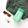 Mint green LoonaGo tucked into a green backpack alongside tortoiseshell sunglasses and keys, styled as an everyday carry essential