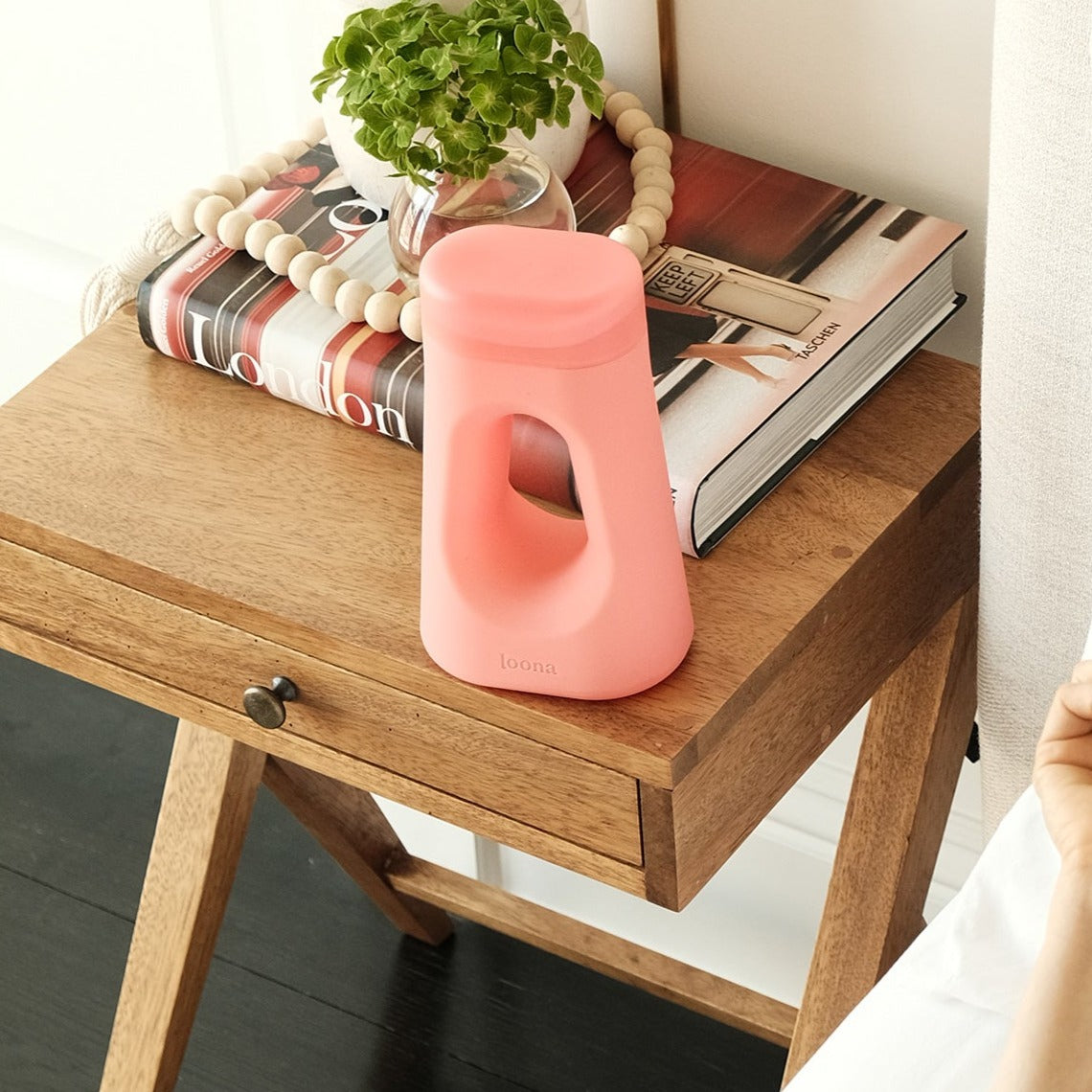 Coral Loona styled on a wooden nightstand alongside a small plant, art book, and decorative wooden beads, blending naturally into bedroom decor