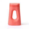Front view of the Loona female urinal in coral pink on a white background, showing the contoured body, integrated handle, and snap-close lid